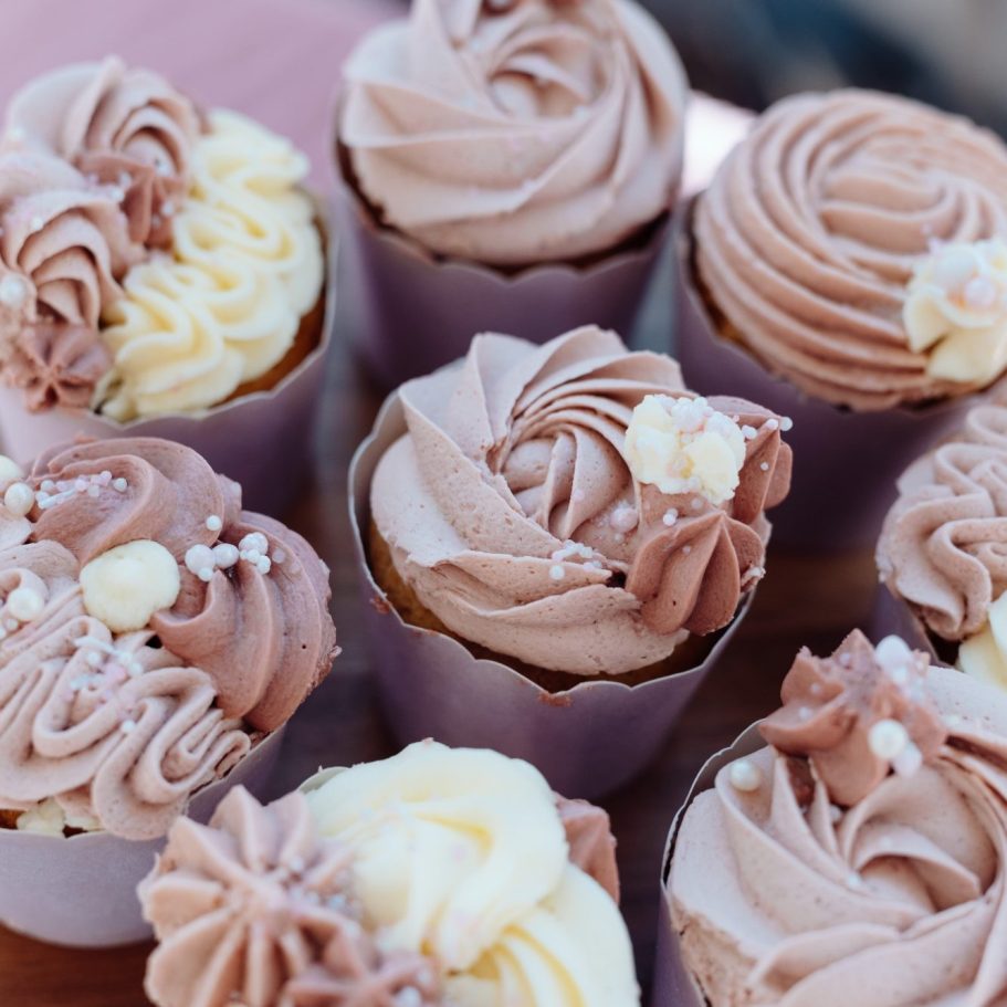 Bunte cupcakes mit verschiedenen Schokoladen- und Vanille-Toppings in Rosa- und Cremetönen.