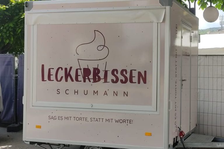 Ein kleiner Verkaufsstand mit dem Namen "Leckerbissen Schumann" in sanften Farben.