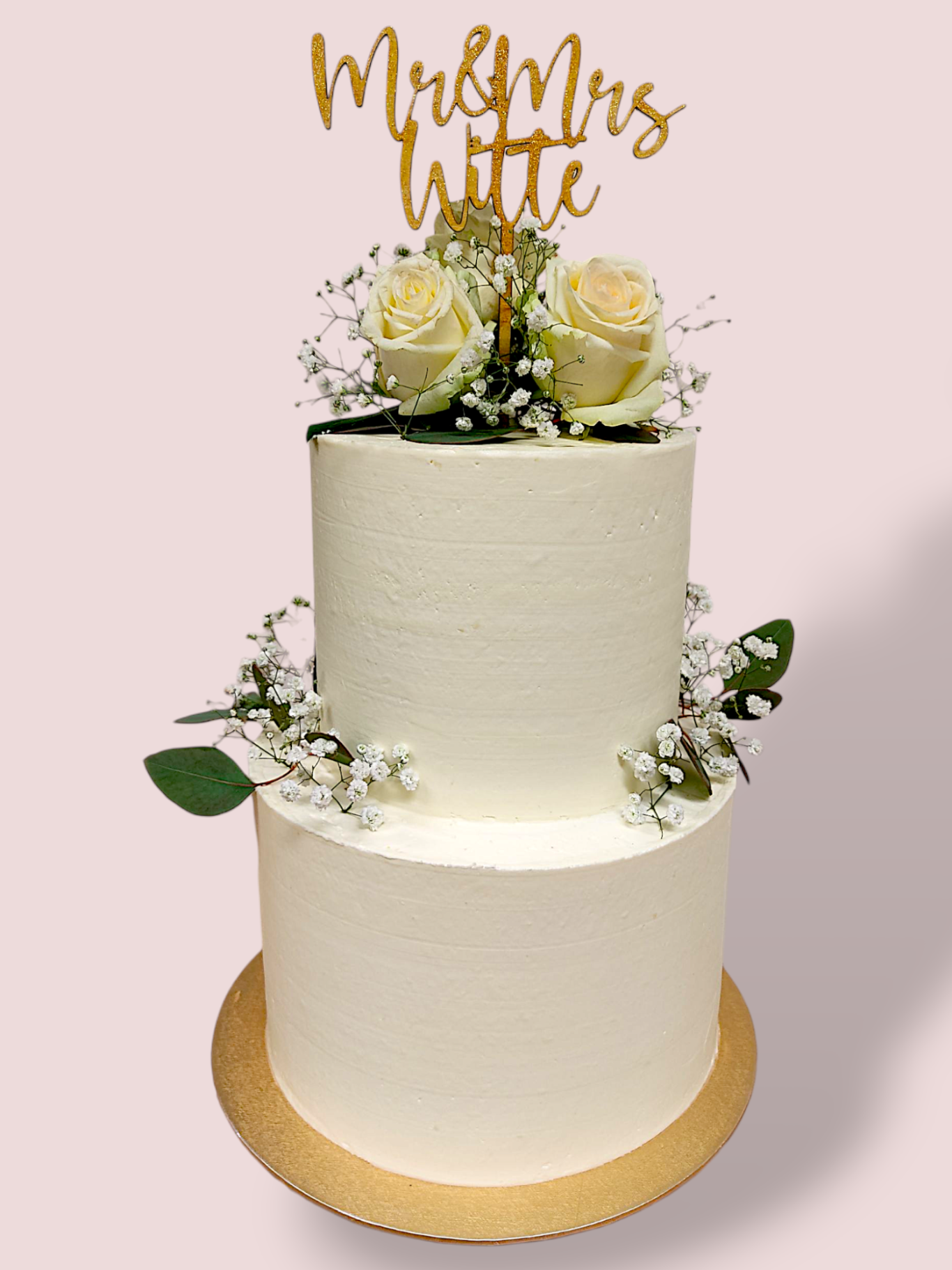 Zweistöckige Hochzeitstorte mit goldener Schrift "Mr & Mrs Witte" und weißen Rosen dekoriert.
