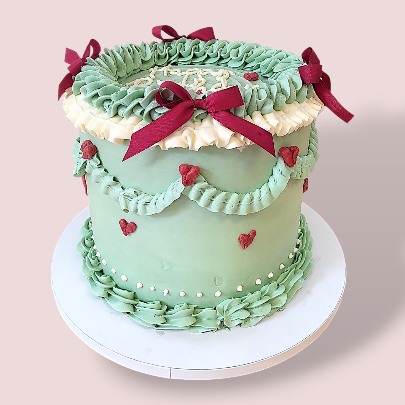 Pastellgrüne Torte mit roten Schleifen, Ruffels und Herzen dekoriert.