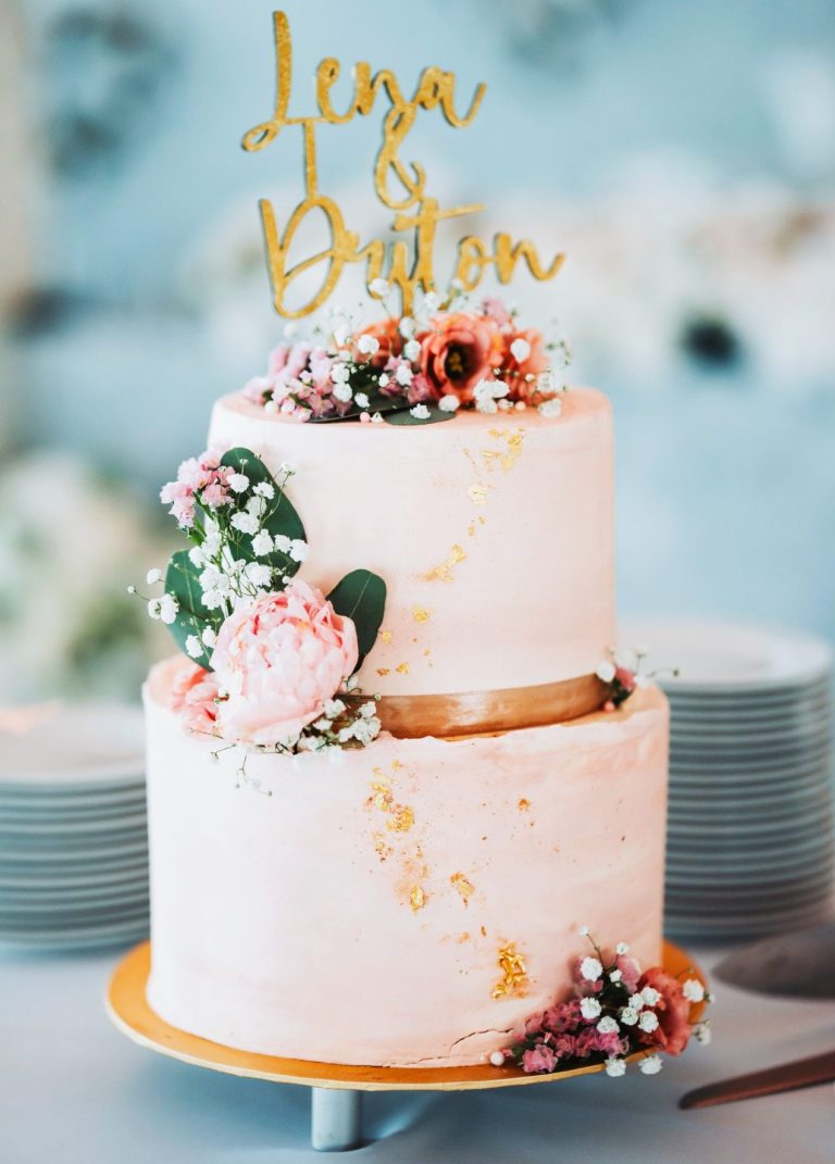 Hochzeitstorte Zweistöckige Hochzeitstorte mit Blüten und goldenem Topper.
