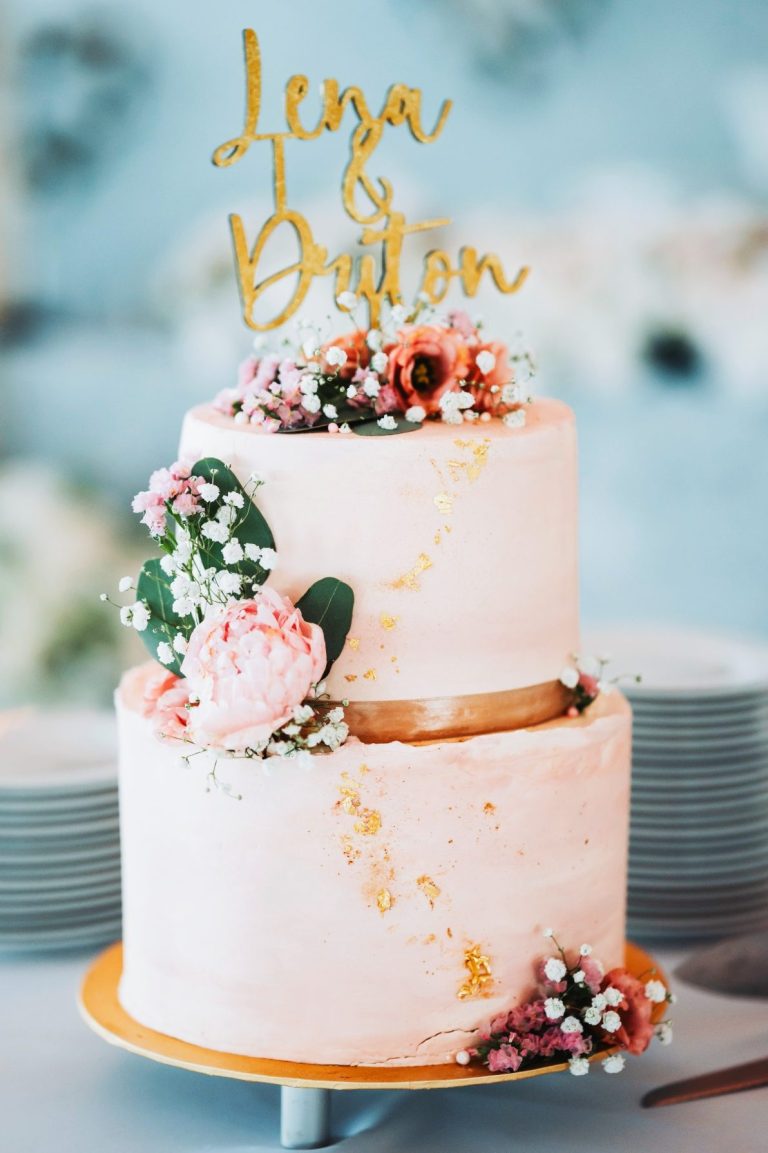 Hochzeitstorte mit goldener Beschriftung und floralen Dekorationen.