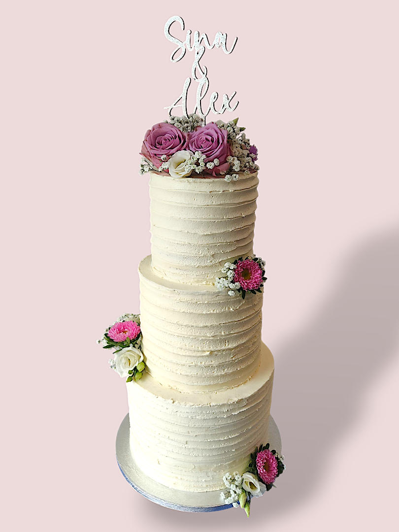 Drei-stöckige Hochzeitstorte mit rosa Blumen und einer dekorativen Cake Topper oben.