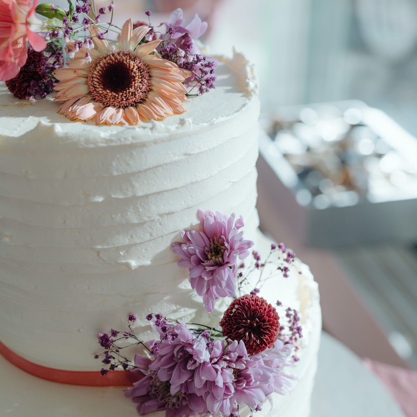 Hochzeitstorte mit weißen Schichten, dekoriert mit Blumen und einer orangefarbenen Schleife.