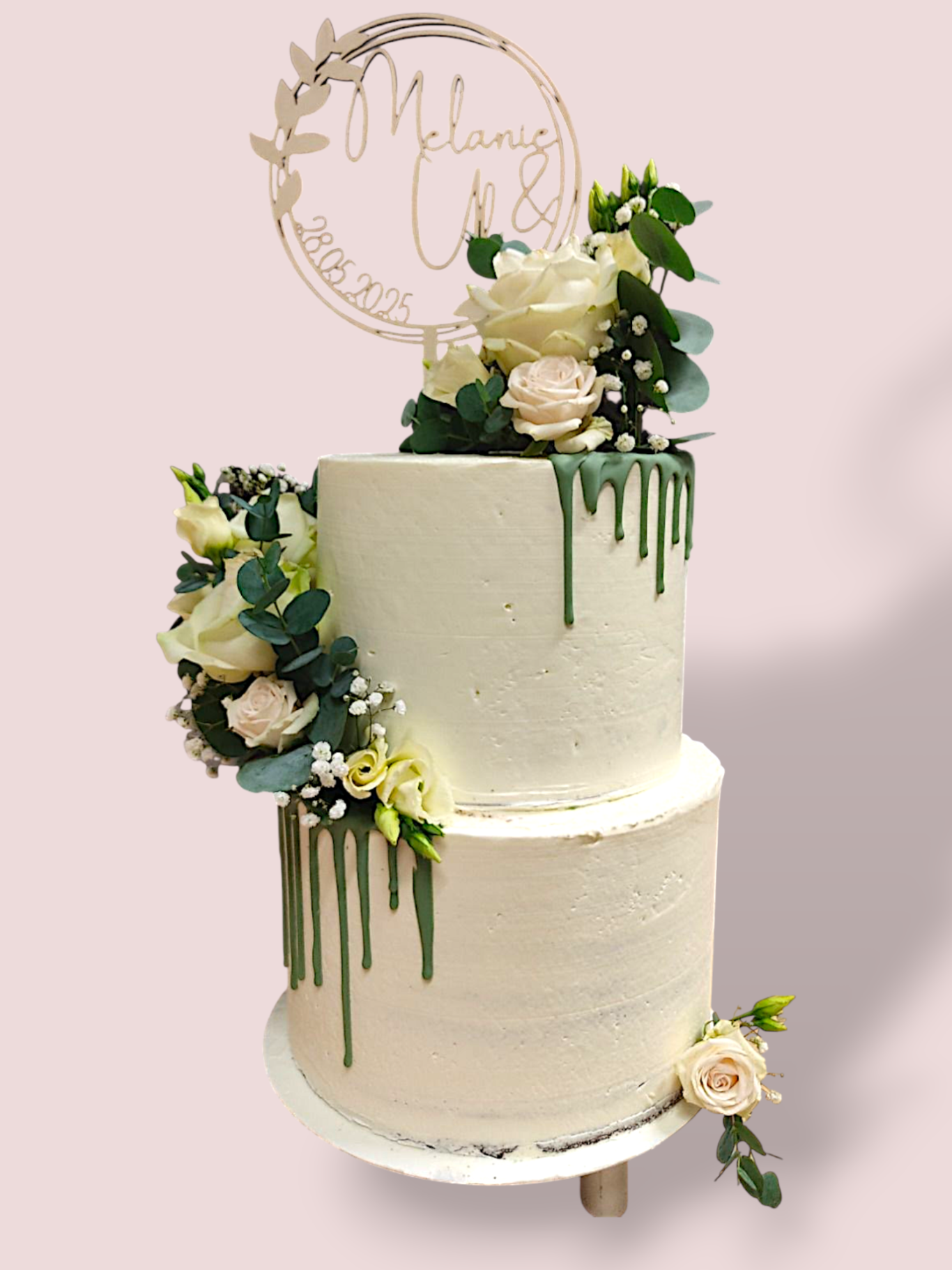 Zweistöckige Hochzeitstorte mit Blumen, Drip und dekorativem Schriftzug oben.