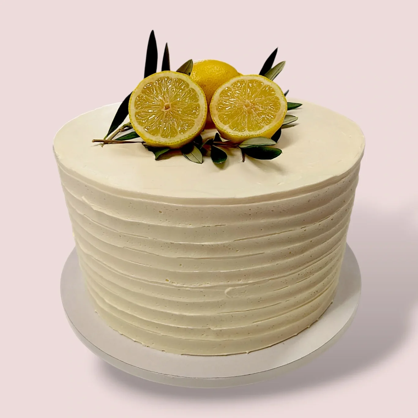 Eine weiße Torte mit Rillen mit einer glatten weißen Creme und dekorativen Zitronenscheiben, sowie Olivenzweige