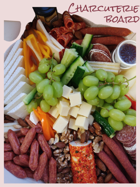 Bunte Auswahl an Wurst, Käse, Trauben, Gurken, Nüssen und Dips auf einer Platte.