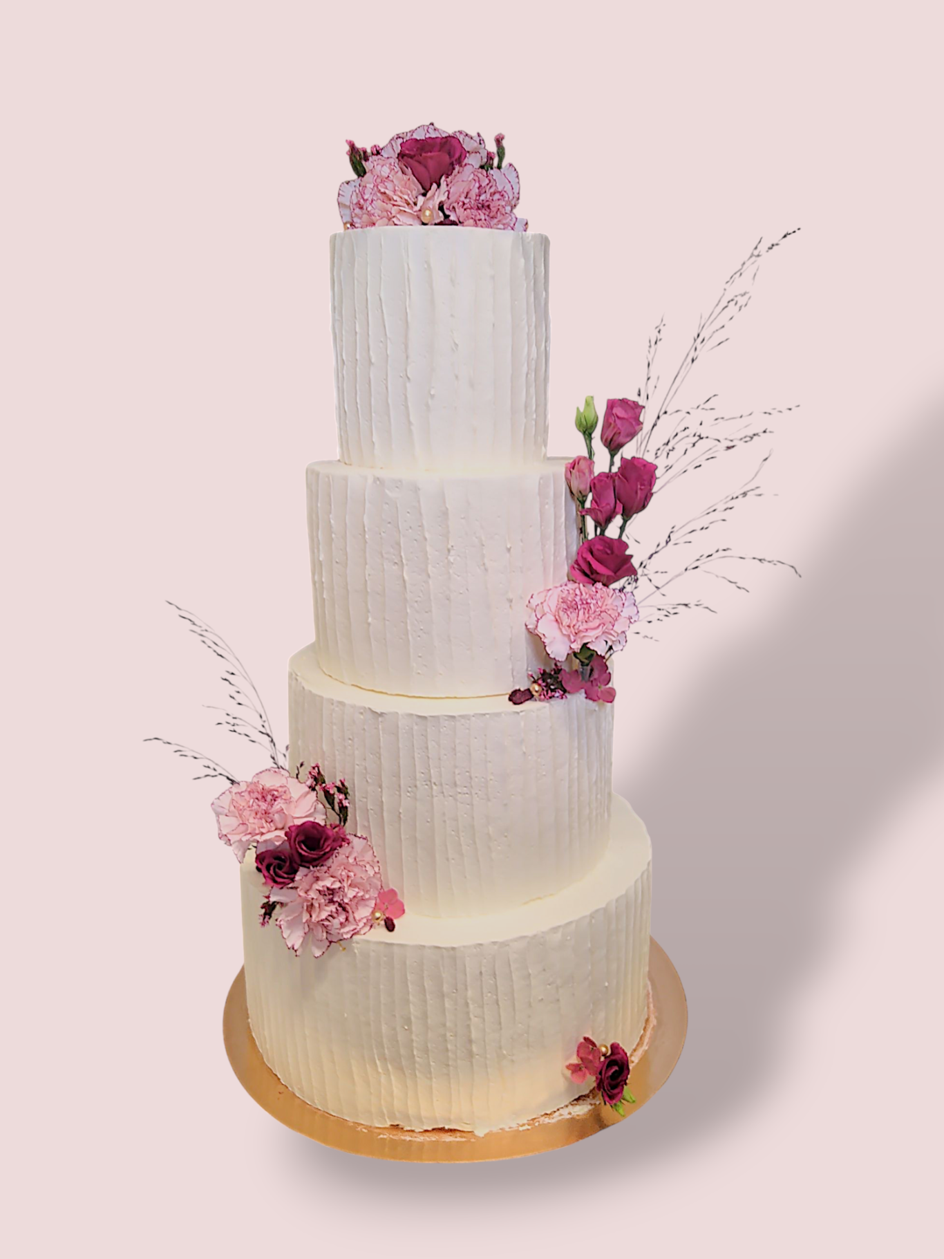 Vieristöckige Hochzeitstorte mit Blumen und dekorativem Schriftzug oben.