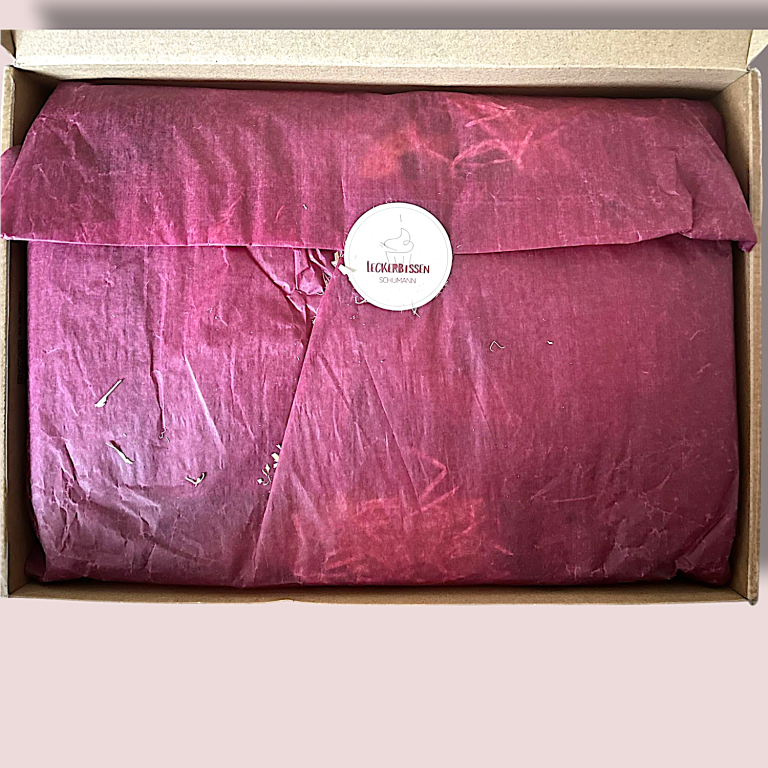 Rotes, eingepacktes Paket in einer braunen Box, mit einem runden Aufkleber.