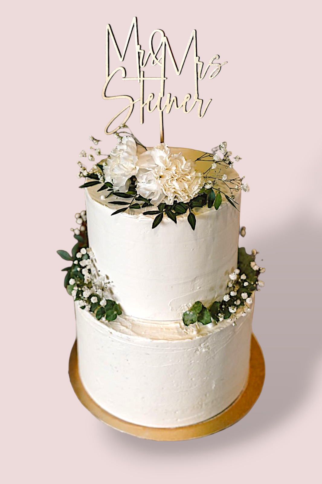 Zweistöckige Hochzeitstorte mit goldener Dekoration und frischen Blumen.